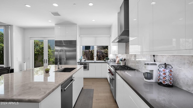 kitchen featuring dark stone countertops, white cabinetry, light hardwood / wood-style flooring, high quality appliances, and wall chimney range hood