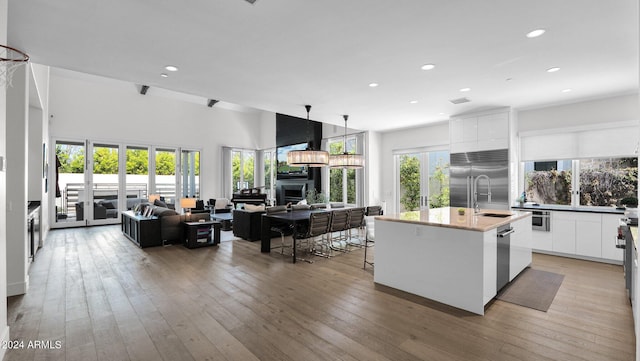 kitchen featuring hanging light fixtures, white cabinets, stainless steel appliances, a center island with sink, and hardwood / wood-style floors