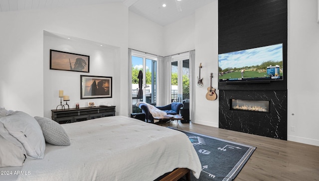 bedroom featuring high vaulted ceiling, wood-type flooring, a premium fireplace, and access to outside