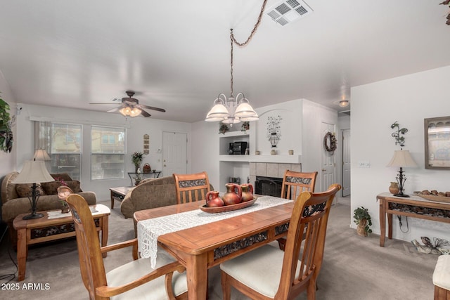 carpeted dining area with a tiled fireplace and ceiling fan with notable chandelier