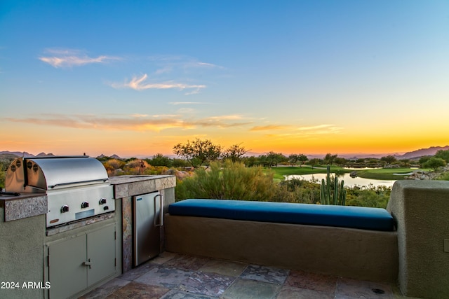 patio terrace at dusk with a water view, grilling area, and a balcony