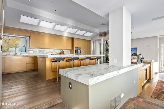 kitchen with a kitchen breakfast bar, backsplash, light hardwood / wood-style flooring, and a kitchen island