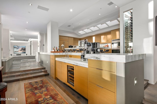 kitchen with a large island, dark hardwood / wood-style floors, light brown cabinetry, and beverage cooler