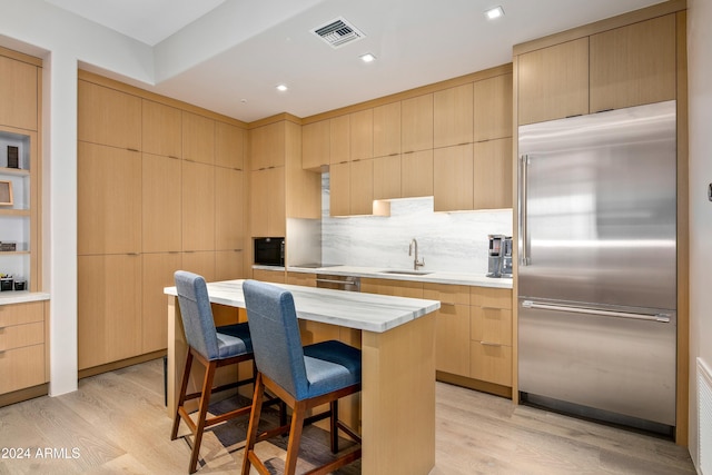 kitchen featuring built in appliances, light hardwood / wood-style floors, sink, and light brown cabinets