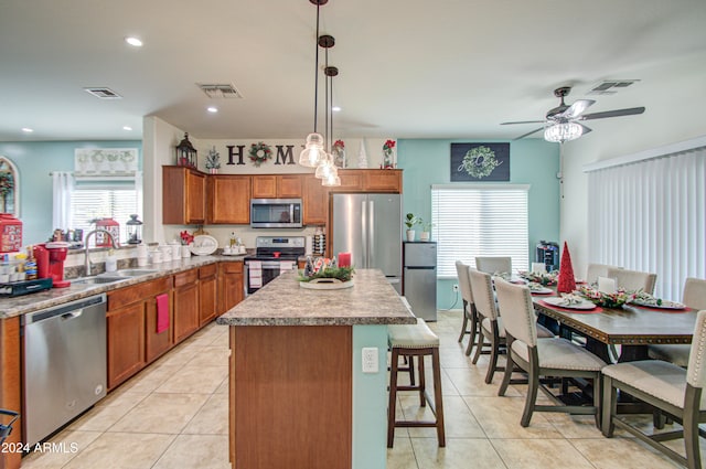 kitchen featuring stainless steel appliances, ceiling fan, sink, a center island, and hanging light fixtures