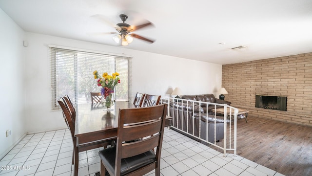 dining room with a brick fireplace, light hardwood / wood-style floors, and ceiling fan