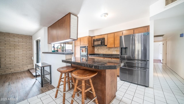 kitchen featuring light tile patterned floors, sink, black appliances, brick wall, and decorative backsplash