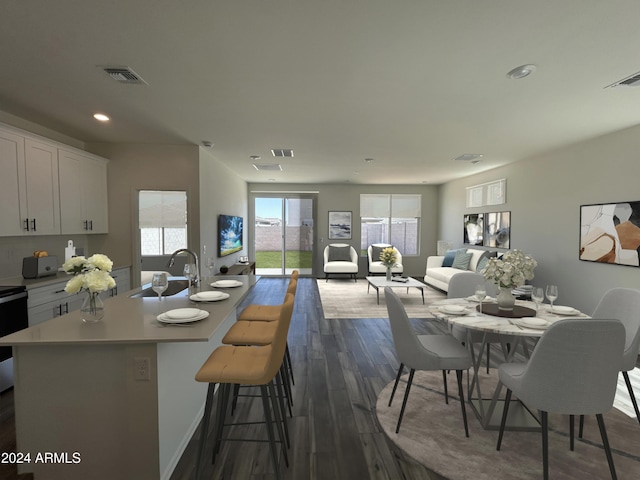 kitchen featuring a kitchen bar, white cabinets, sink, dark hardwood / wood-style flooring, and an island with sink