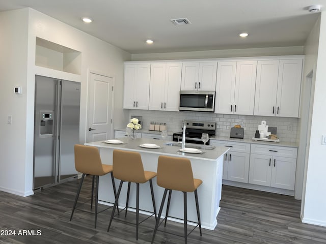 kitchen featuring a kitchen breakfast bar, a center island with sink, white cabinetry, and appliances with stainless steel finishes