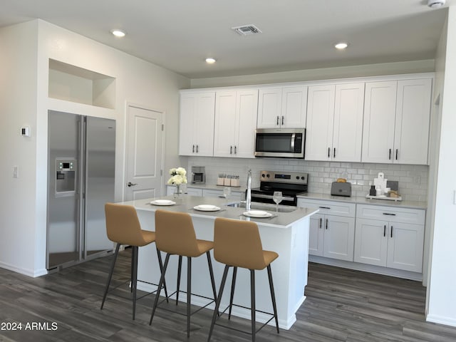 kitchen with white cabinets, a center island with sink, appliances with stainless steel finishes, and decorative backsplash