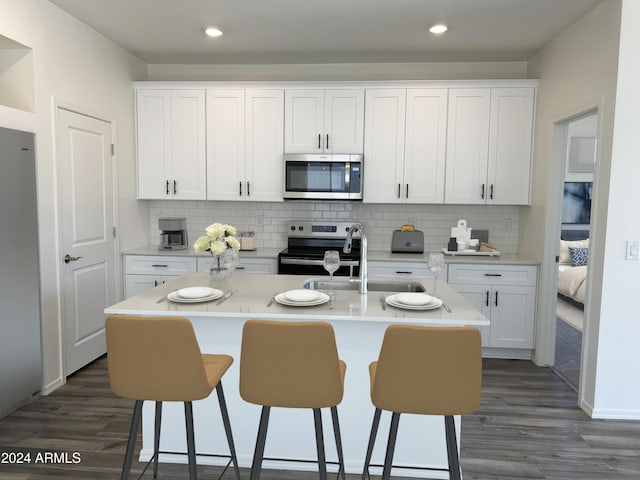 kitchen with decorative backsplash, white cabinets, appliances with stainless steel finishes, and a kitchen island with sink