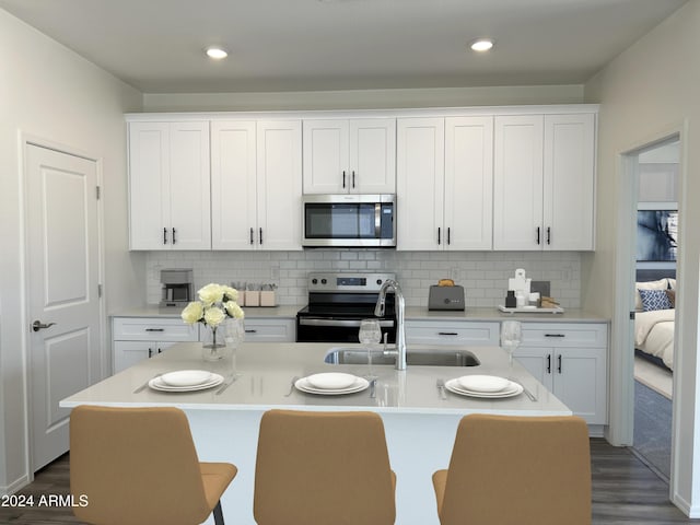 kitchen featuring a kitchen island with sink, white cabinetry, tasteful backsplash, and appliances with stainless steel finishes