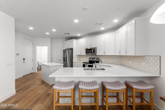 kitchen with light hardwood / wood-style flooring, a breakfast bar, stainless steel appliances, white cabinets, and kitchen peninsula