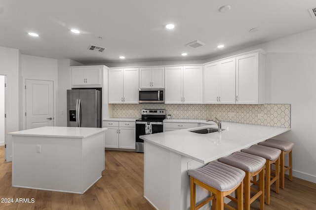 kitchen featuring a kitchen bar, sink, kitchen peninsula, stainless steel appliances, and white cabinets