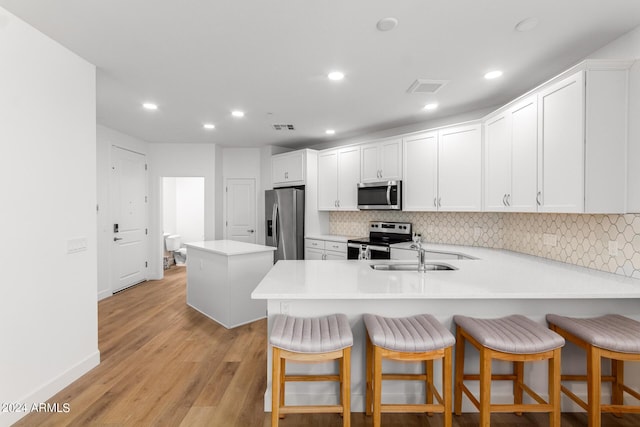 kitchen with a kitchen bar, sink, kitchen peninsula, stainless steel appliances, and white cabinets