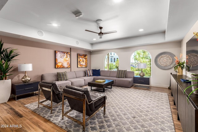 living room featuring a tray ceiling, ceiling fan, and light wood-type flooring