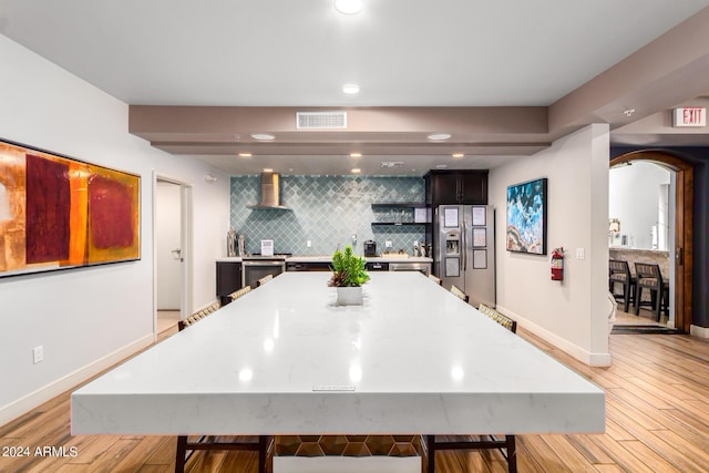 kitchen featuring a breakfast bar area, backsplash, a center island, light hardwood / wood-style floors, and wall chimney range hood