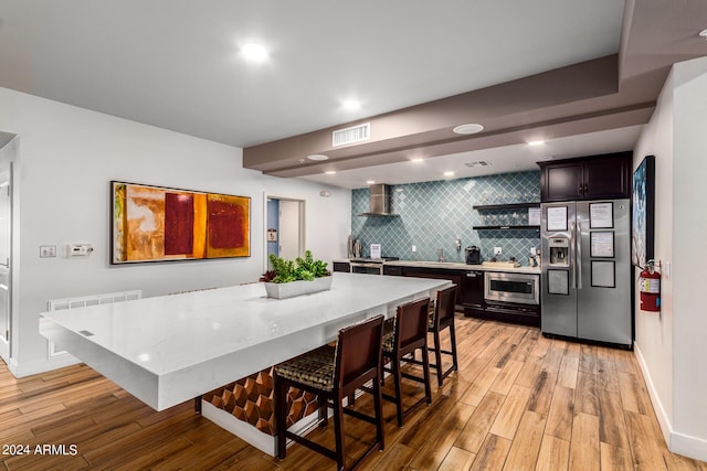 kitchen featuring a breakfast bar area, a center island, light hardwood / wood-style flooring, stainless steel appliances, and wall chimney range hood