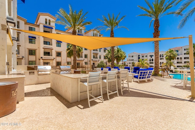 view of patio with a community pool, an outdoor wet bar, grilling area, and an outdoor kitchen