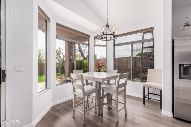 dining space featuring baseboards, wood finished floors, a chandelier, and vaulted ceiling