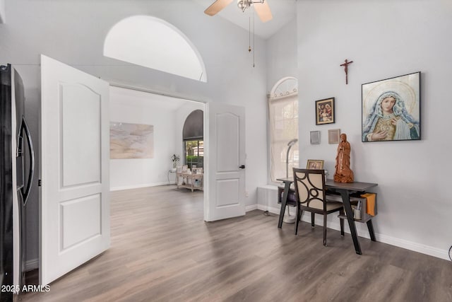 interior space with arched walkways, a high ceiling, baseboards, and wood finished floors