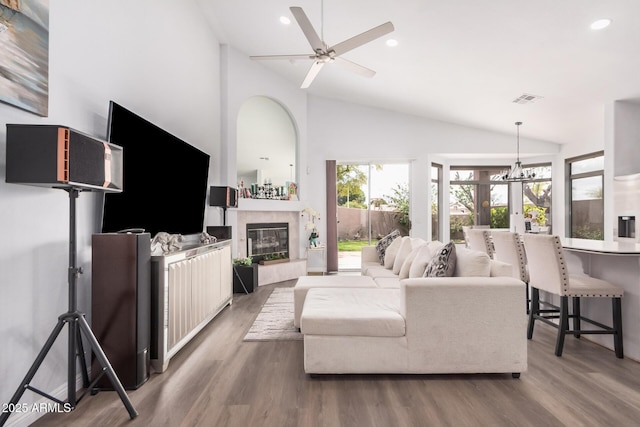 living room featuring a tiled fireplace, visible vents, ceiling fan with notable chandelier, and wood finished floors