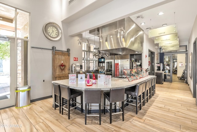 kitchen with a towering ceiling, a breakfast bar area, light stone counters, a barn door, and high end fridge