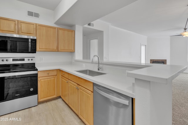 kitchen with appliances with stainless steel finishes, light brown cabinetry, kitchen peninsula, and sink