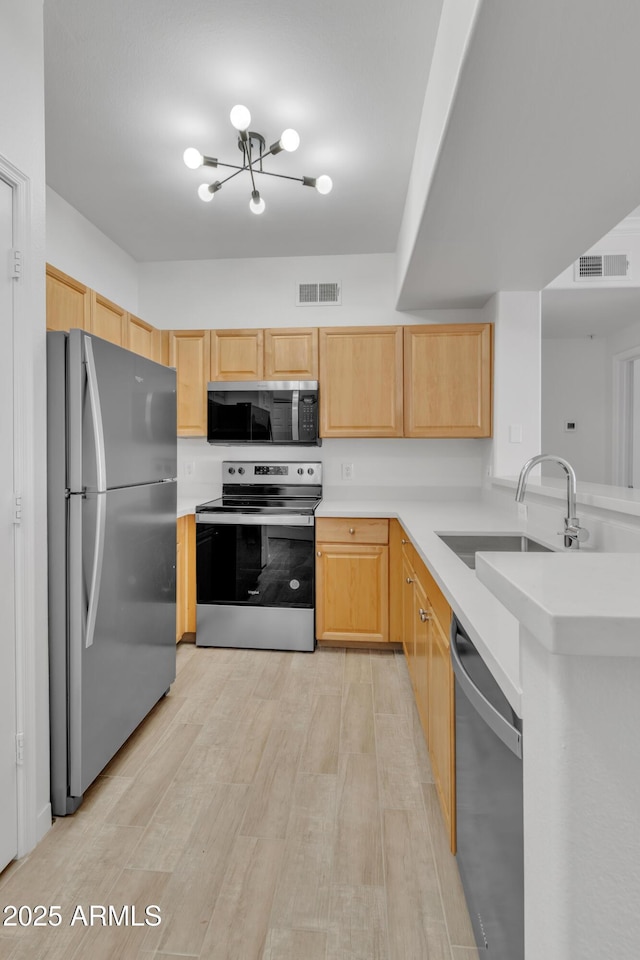 kitchen with appliances with stainless steel finishes, sink, kitchen peninsula, light brown cabinets, and light wood-type flooring