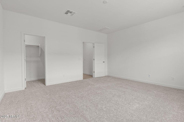 unfurnished bedroom featuring a walk in closet, a closet, light colored carpet, visible vents, and baseboards