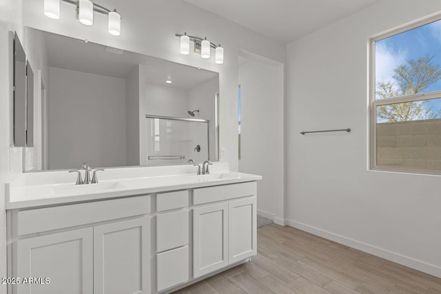 bathroom featuring wood finished floors, a sink, baseboards, double vanity, and a stall shower