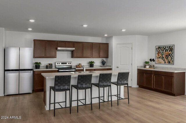 kitchen with appliances with stainless steel finishes, light countertops, light wood-type flooring, under cabinet range hood, and a sink