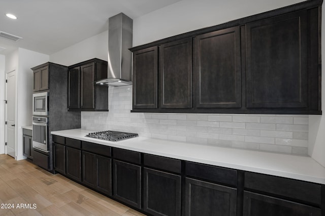 kitchen featuring wall chimney exhaust hood, stainless steel appliances, light hardwood / wood-style floors, and tasteful backsplash