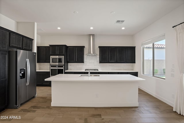 kitchen featuring a center island with sink, appliances with stainless steel finishes, sink, and wall chimney range hood