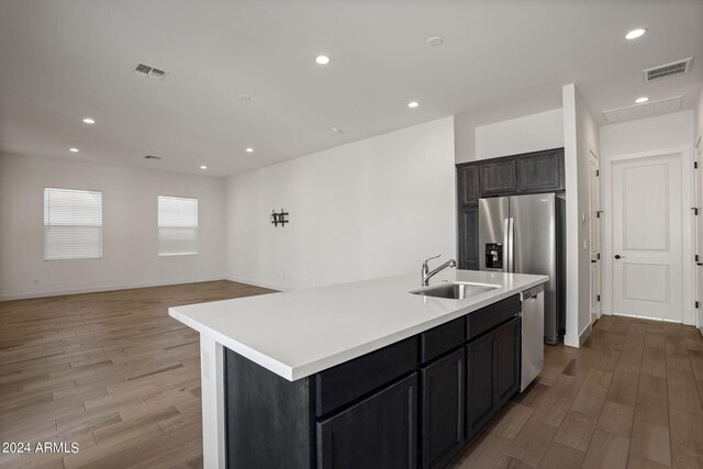 kitchen with wall chimney exhaust hood, appliances with stainless steel finishes, a kitchen island with sink, and sink