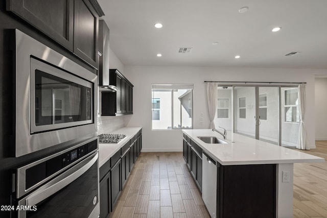 kitchen featuring an island with sink, appliances with stainless steel finishes, sink, and light hardwood / wood-style flooring