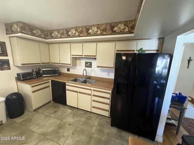 kitchen featuring cream cabinetry, light countertops, a sink, and black appliances