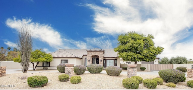 mediterranean / spanish house with stone siding, stucco siding, a tile roof, and fence