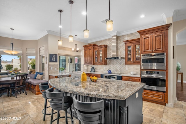 kitchen with brown cabinetry, visible vents, decorative backsplash, wall chimney exhaust hood, and a center island