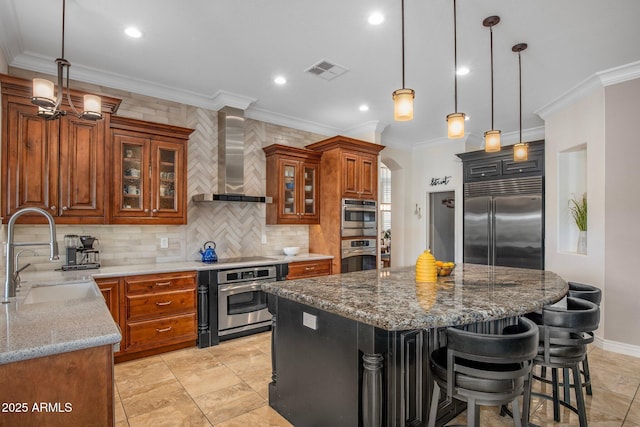 kitchen with visible vents, wall chimney range hood, brown cabinets, stainless steel appliances, and a sink