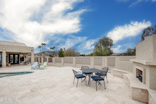 view of patio with an outdoor stone fireplace, outdoor dining space, and fence