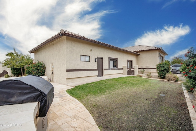 back of house featuring fence, a tiled roof, stucco siding, a lawn, and a patio area