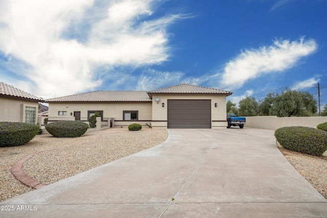 view of front of home featuring fence, a tiled roof, concrete driveway, stucco siding, and an attached garage