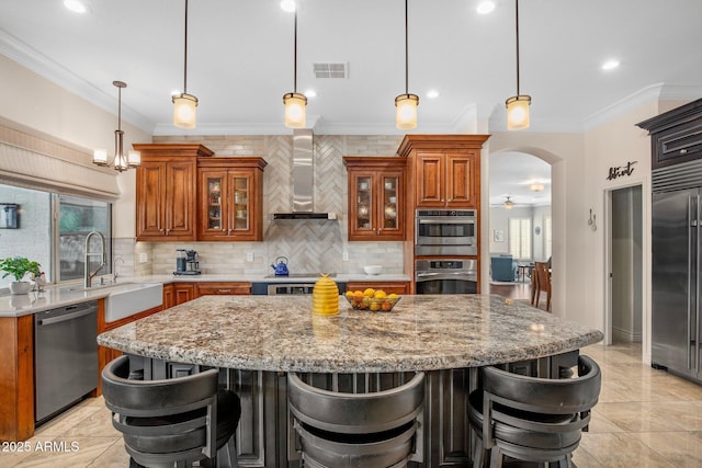 kitchen featuring brown cabinetry, visible vents, stainless steel appliances, wall chimney range hood, and a center island