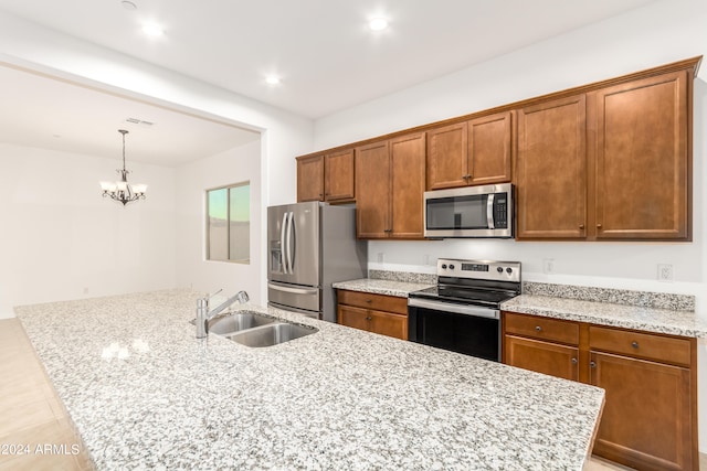 kitchen featuring decorative light fixtures, sink, light stone countertops, an island with sink, and appliances with stainless steel finishes