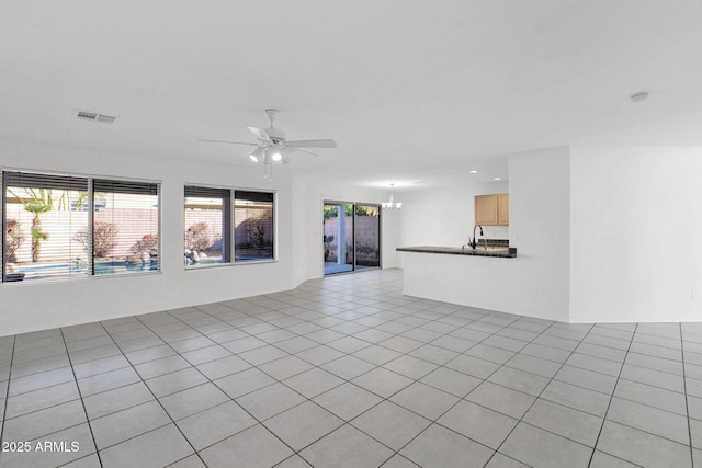 unfurnished living room featuring light tile patterned flooring, plenty of natural light, sink, and ceiling fan with notable chandelier