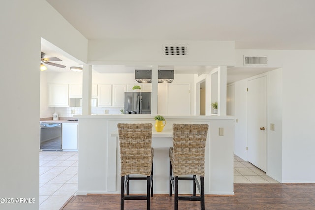 kitchen with dishwashing machine, stainless steel fridge, white cabinets, and visible vents