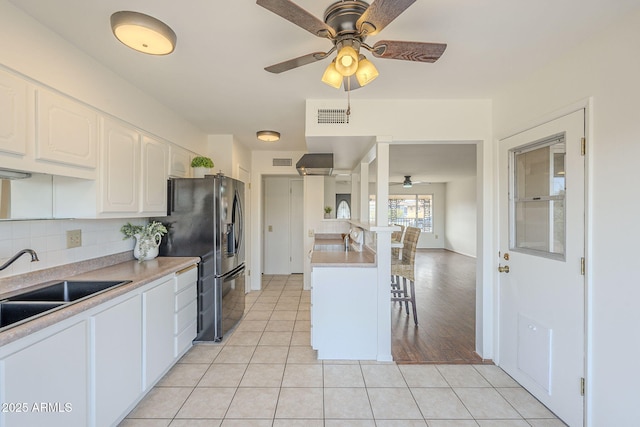 kitchen with visible vents, a breakfast bar, light countertops, light tile patterned flooring, and a sink