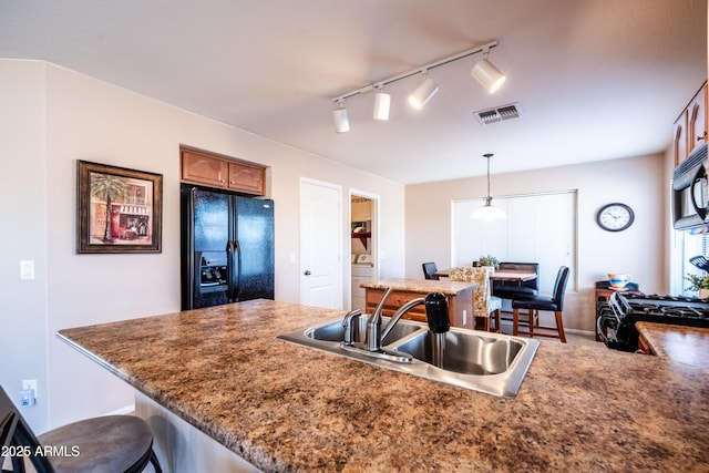 kitchen featuring visible vents, brown cabinets, black appliances, a kitchen bar, and a sink