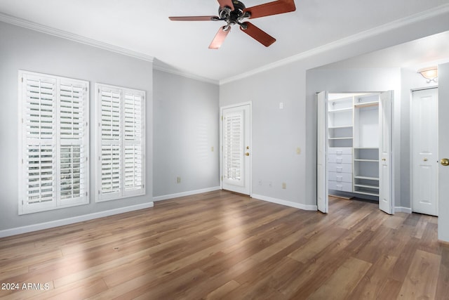 unfurnished bedroom featuring ceiling fan, hardwood / wood-style floors, crown molding, and two closets